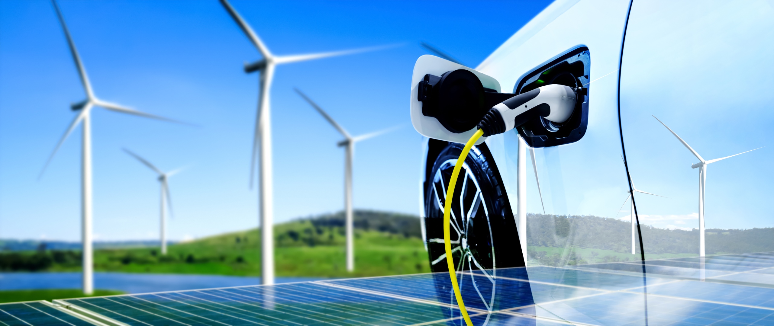 Coche eléctrico cargando al lado de una placa solar y un molino de viento